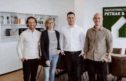 Pascal Groß, Margret Giese, Laurin Petrak und Christopher Eisele im Besprechungszimmer vor dem großen Tisch und dem Firmenlogo in grün an der Wand.