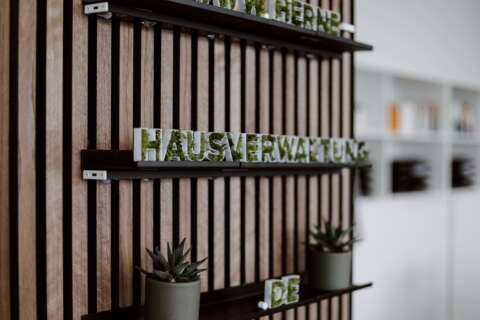 Pflanzen und das Wort Hausverwaltung in begrünten Buchstaben auf einem Regal an der Wand.
