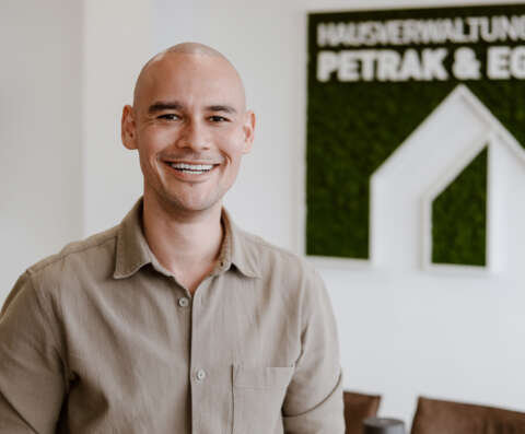 Christopher Eisele im Porträt vor weißer Wand und dem Firmenlogo der Hausverwaltung.