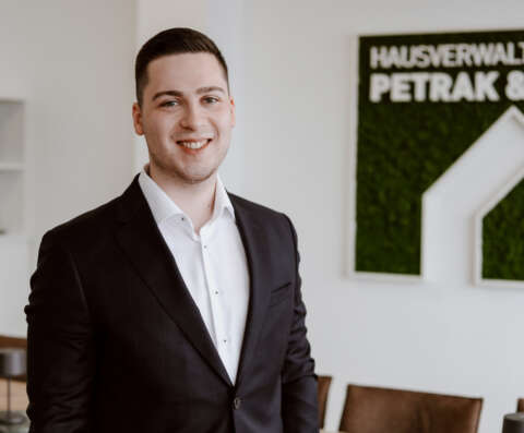 Laurin Petrak im Porträt vor weißer Wand und dem Firmenlogo der Hausverwaltung.