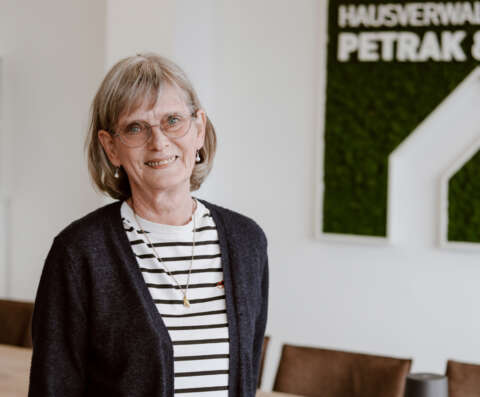 Margret Giese im Porträt vor weißer Wand und dem Firmenlogo der Hausverwaltung.