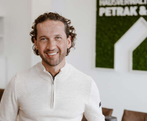 Pascal Groß m Porträt vor weißer Wand und dem Firmenlogo der Hausverwaltung.